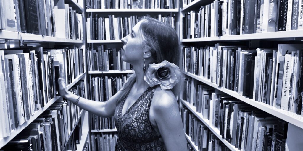 Franziska Ruprecht steht in der Bibliothek des Poets` House New York und schaut auf die Gedichtbände. Sie trägt eine Blume hinter dem Ohr und ein schulterfreies Kleid.